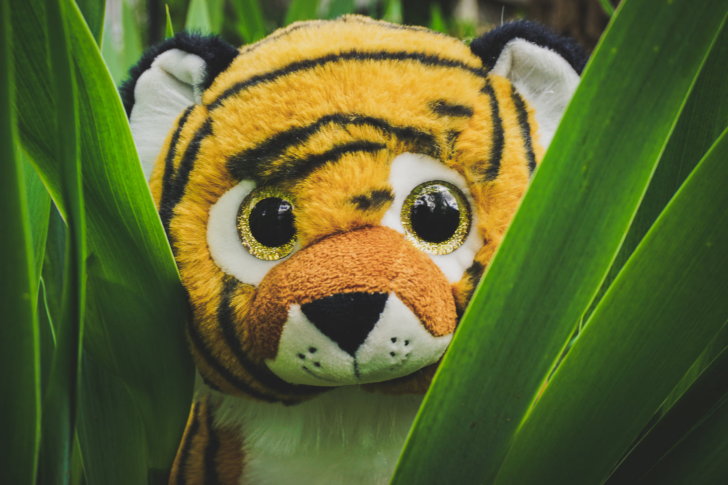 A soft, 16” plush tiger stuffy closeup of it's head peaking through green blades of tall grass. *Comes unstuffed.